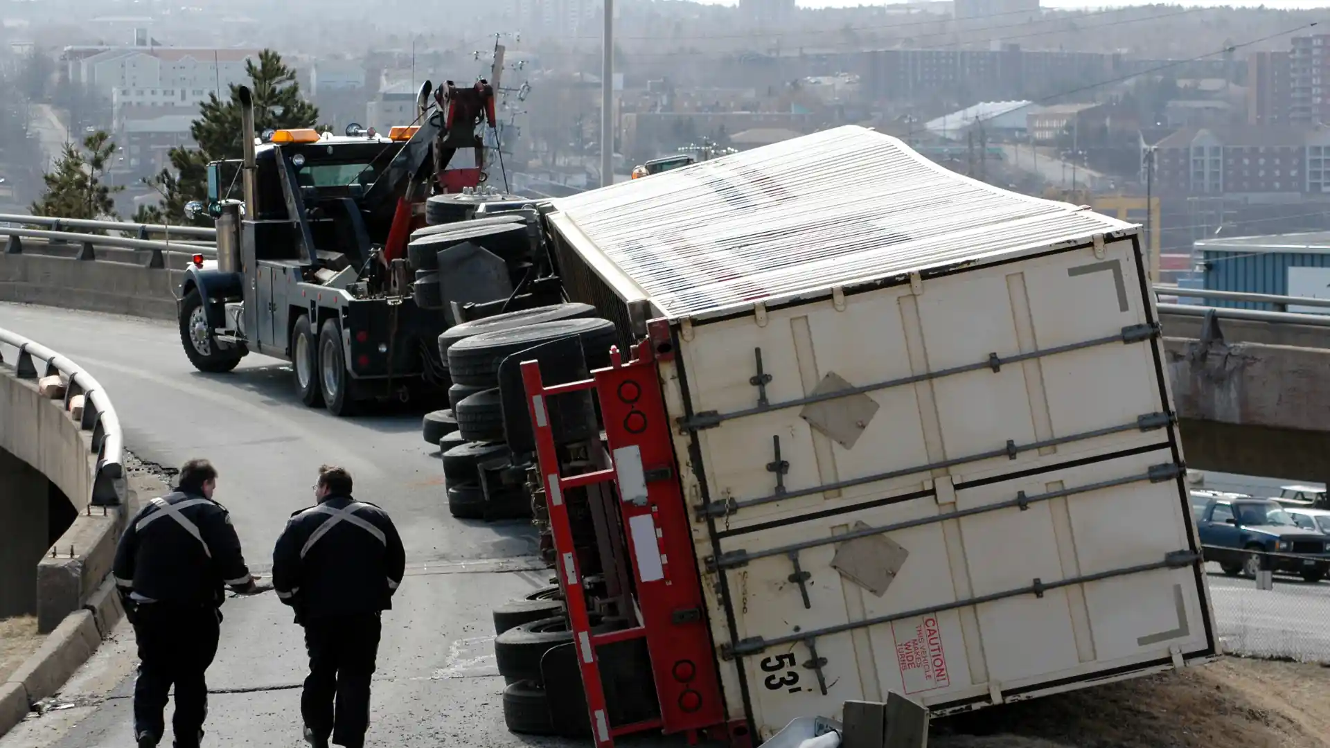 Truck tipped over on the side of the road with a tow truck in the background