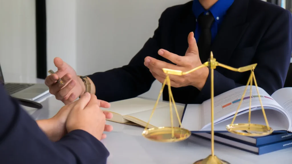 Lawyer speaking with a client at a desk with a scale of justice in the foreground.