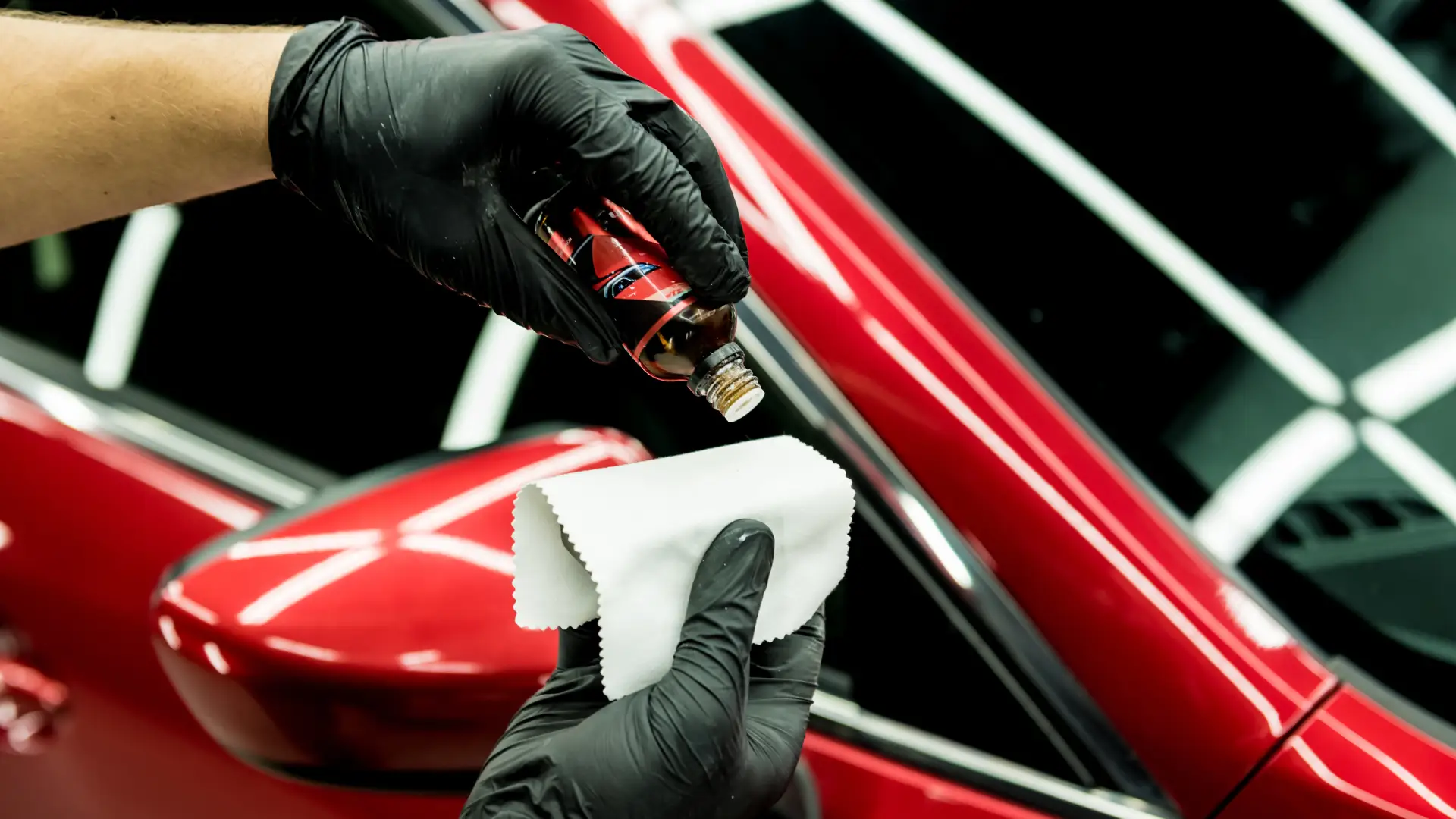 Detailer applying ceramic coating to a red car using a cloth and dropper.