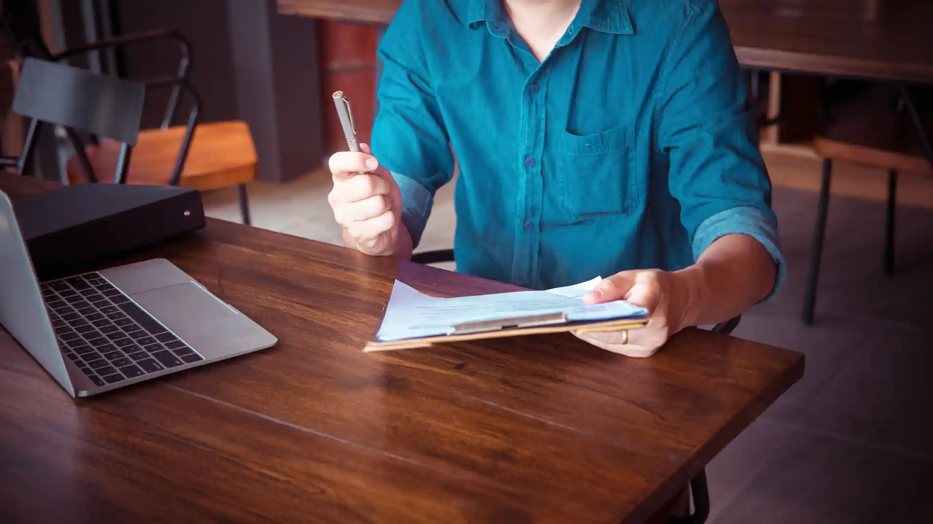 Person holding a clipboard and pen while sitting at a desk.