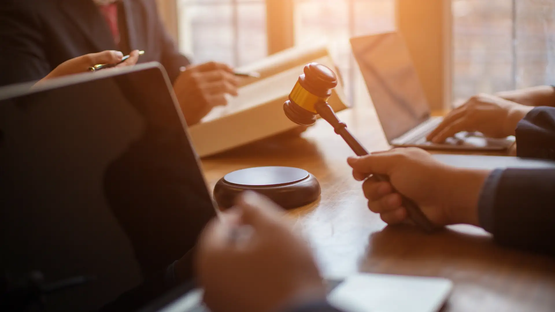Person holding a gavel during a legal discussion at a desk with documents and laptops.