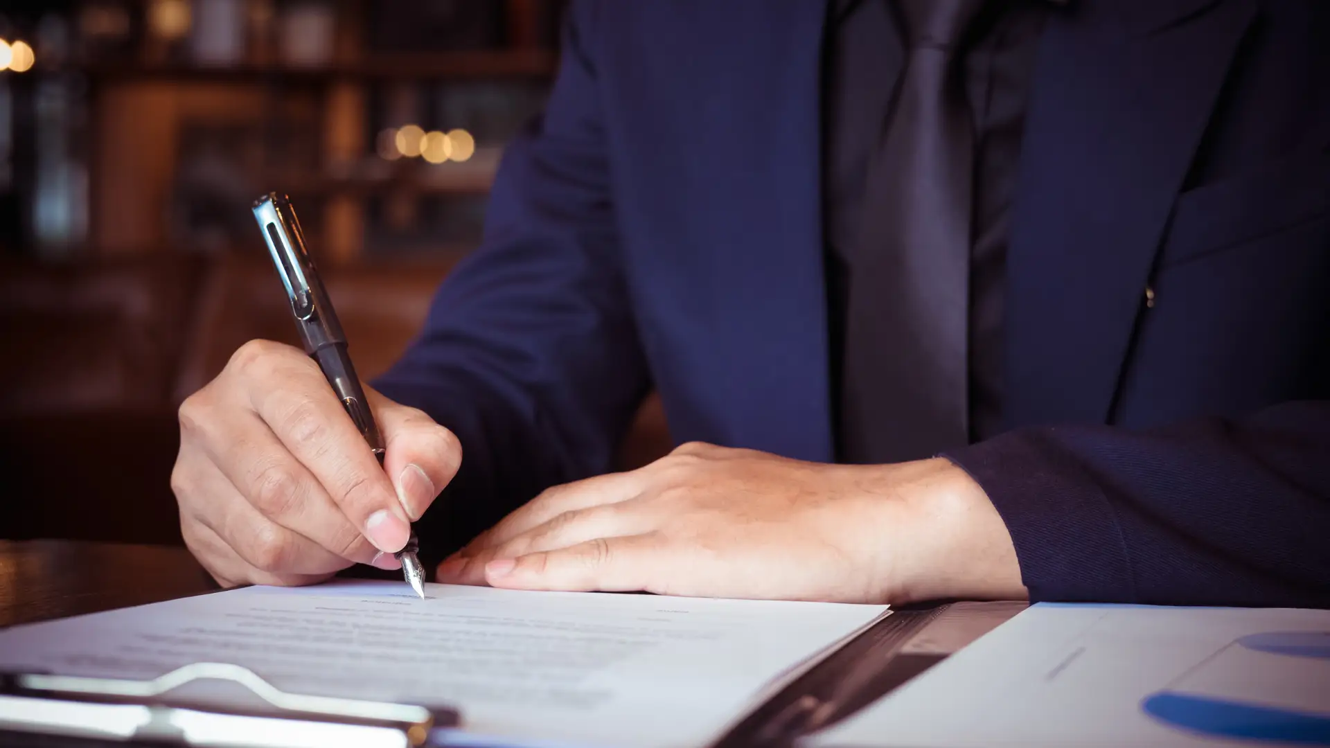 Person in a suit signing a document at a desk.